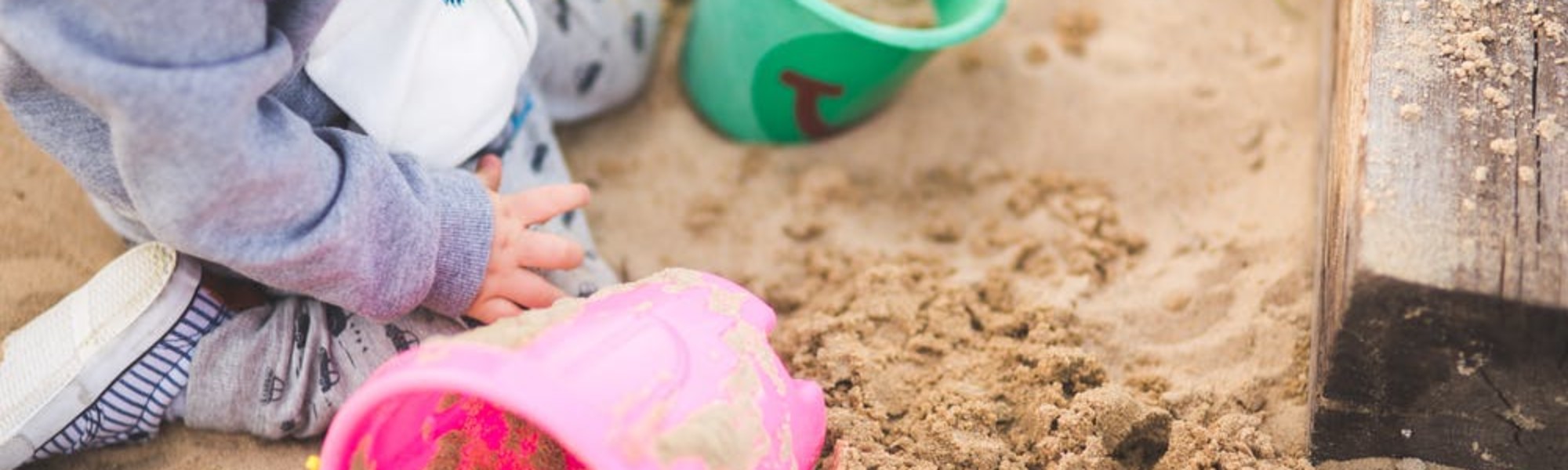 Kuvassa lapsi istuu ämpäreitä ympärillään hiekkalaatikollla.