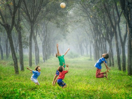 Kuvassa on neljä ilmaan hyppäävää iloista lasta vihreän luonnon keskellä.