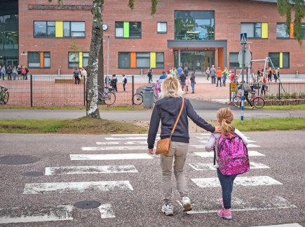 Ekaluokkalainen ylittämässä suojatietä kouluun saattajan kanssa.