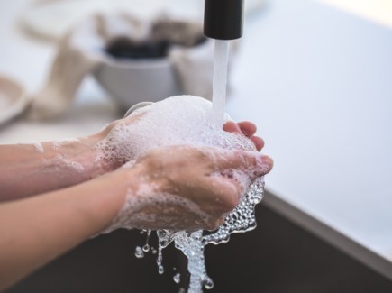 Kuvassa näkyy saippuoidut kädet juoksevan vesihanan alla.