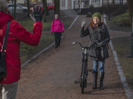 Nainen taluttaa pyörää ja tervehtii vastaantulijaa kädellä