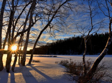 Kuvassa aurinko kultaa lumen peittämän peltomaiseman.