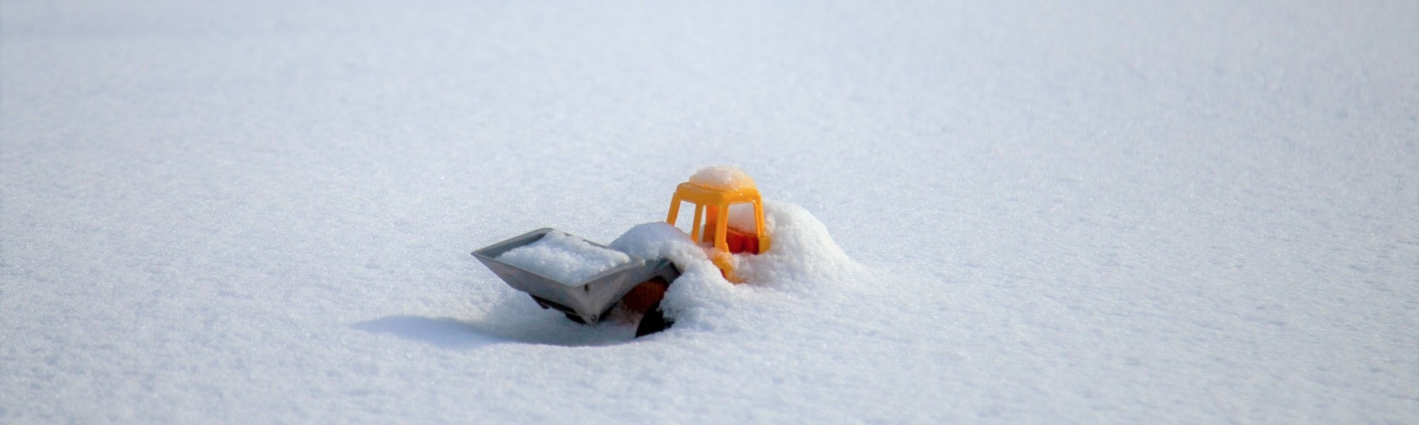 Pieni keltainen muovitraktori on hautautunut vastasataneeseen lumeen.