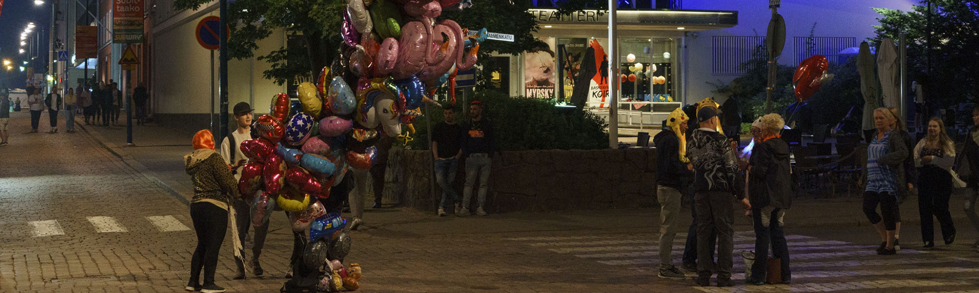 Ilmapallojen myyjä ja ihmisiä teatterin edessä illalla Meripäivillä.