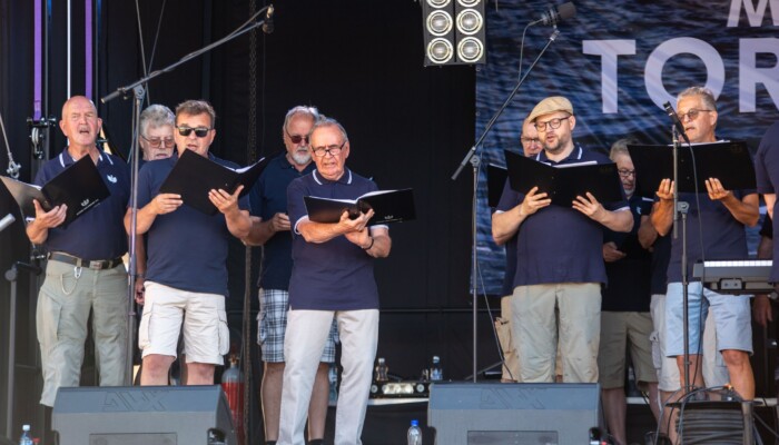 Kotkan Laulumiehet lavalla laulamassa kansioista.