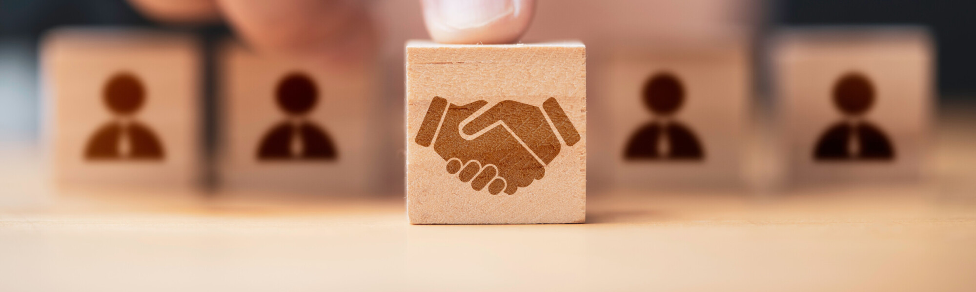 kuvassa sormi osoittaa puu palikkaa jossa on kättelevien ihmisten kuvio