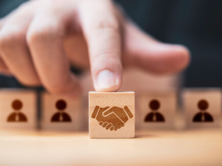 kuvassa sormi osoittaa puu palikkaa jossa on kättelevien ihmisten kuvio