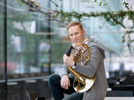Jukka Harju istuu pöydällä soitin kainalossa.