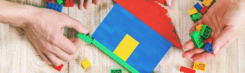 kädet rakentavat Legoista taloa