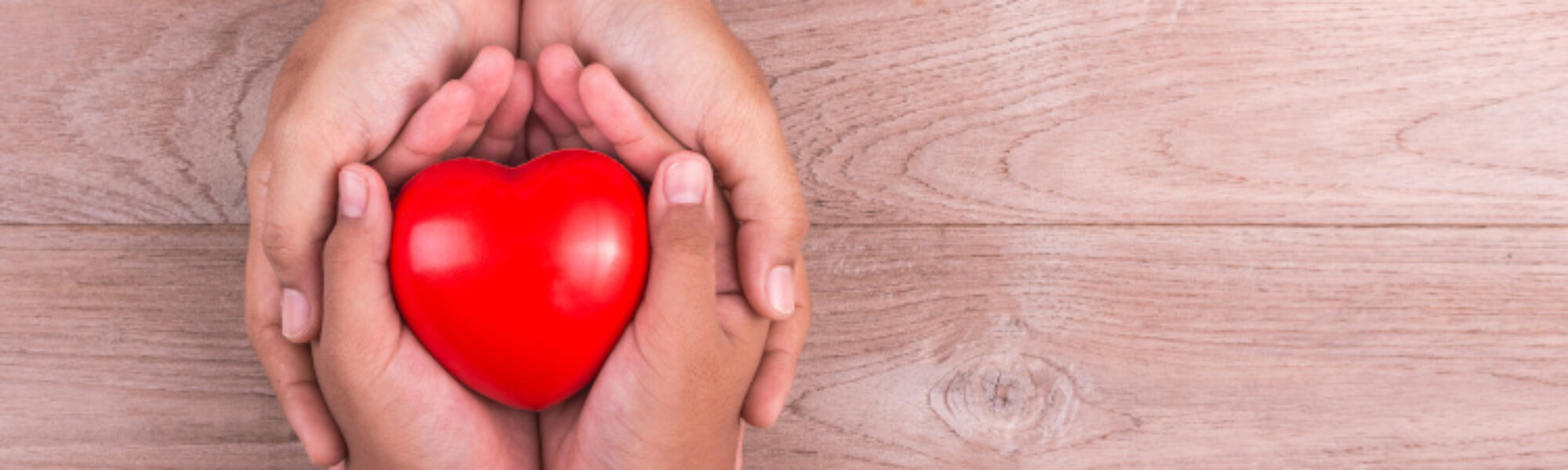 aikuisen kädet pitelevät lapsen kädestä kiinni, keskellä punainen sydän