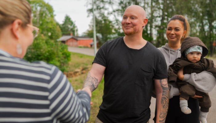 Mies kättelee kaupanteon merkiksi. Nainen vauva sylissä hymyilee hänen takana.