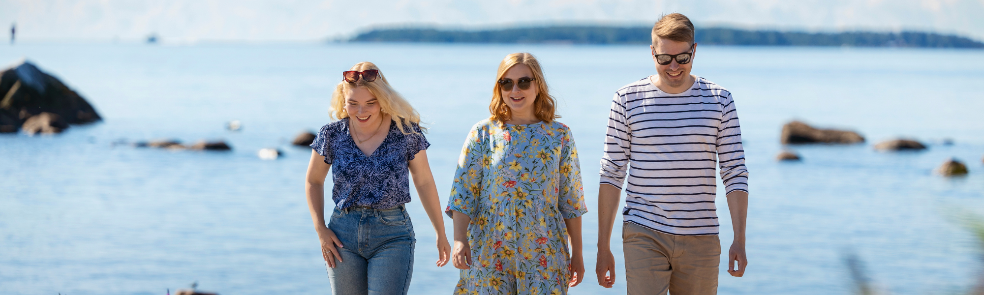 Kolme ihmistä kävelee kameraa kohti. Taustalla saaristomaisemaa ja meri.
